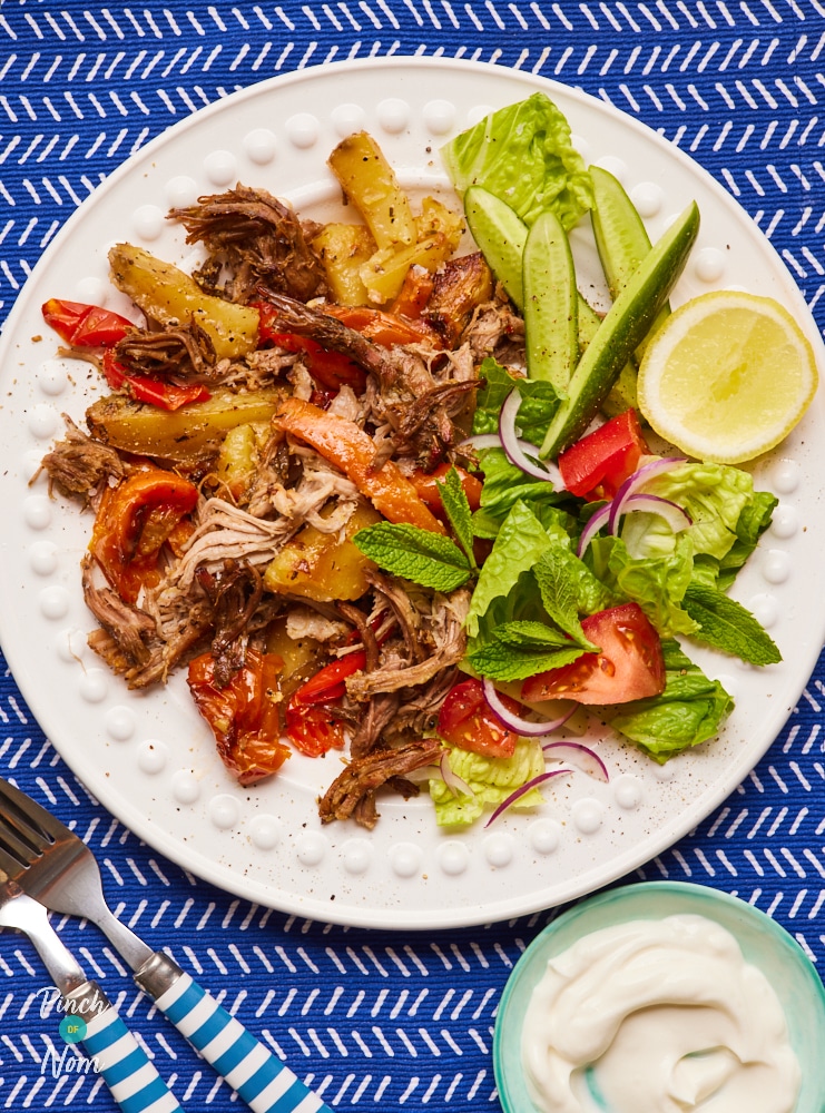 A table is set with a colourful plate of Pinch of Nom's slimming-friendly Kleftiko Lamb. The shredded lamb is served with a crispy, fresh side salad and a small bowl of sauce.
