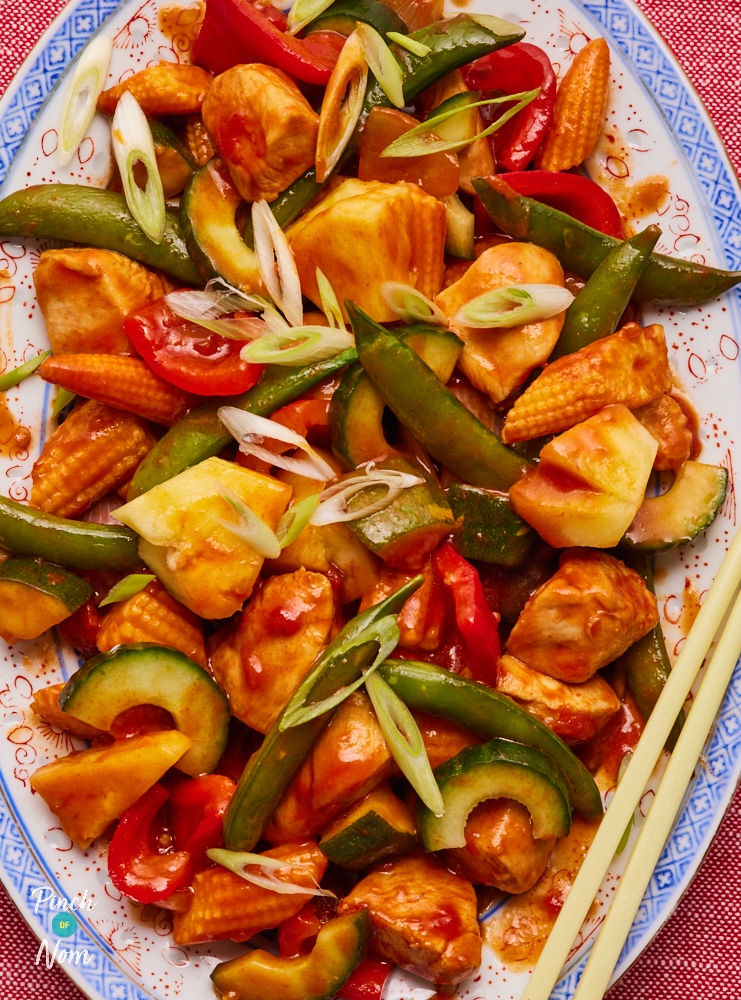 Pinch of Nom's slimming-friendly Sweet and Sour Chicken fakeaway is served at the centre of a table topped with crunchy spring onions. Chopsticks wait to the side, ready to dig in.