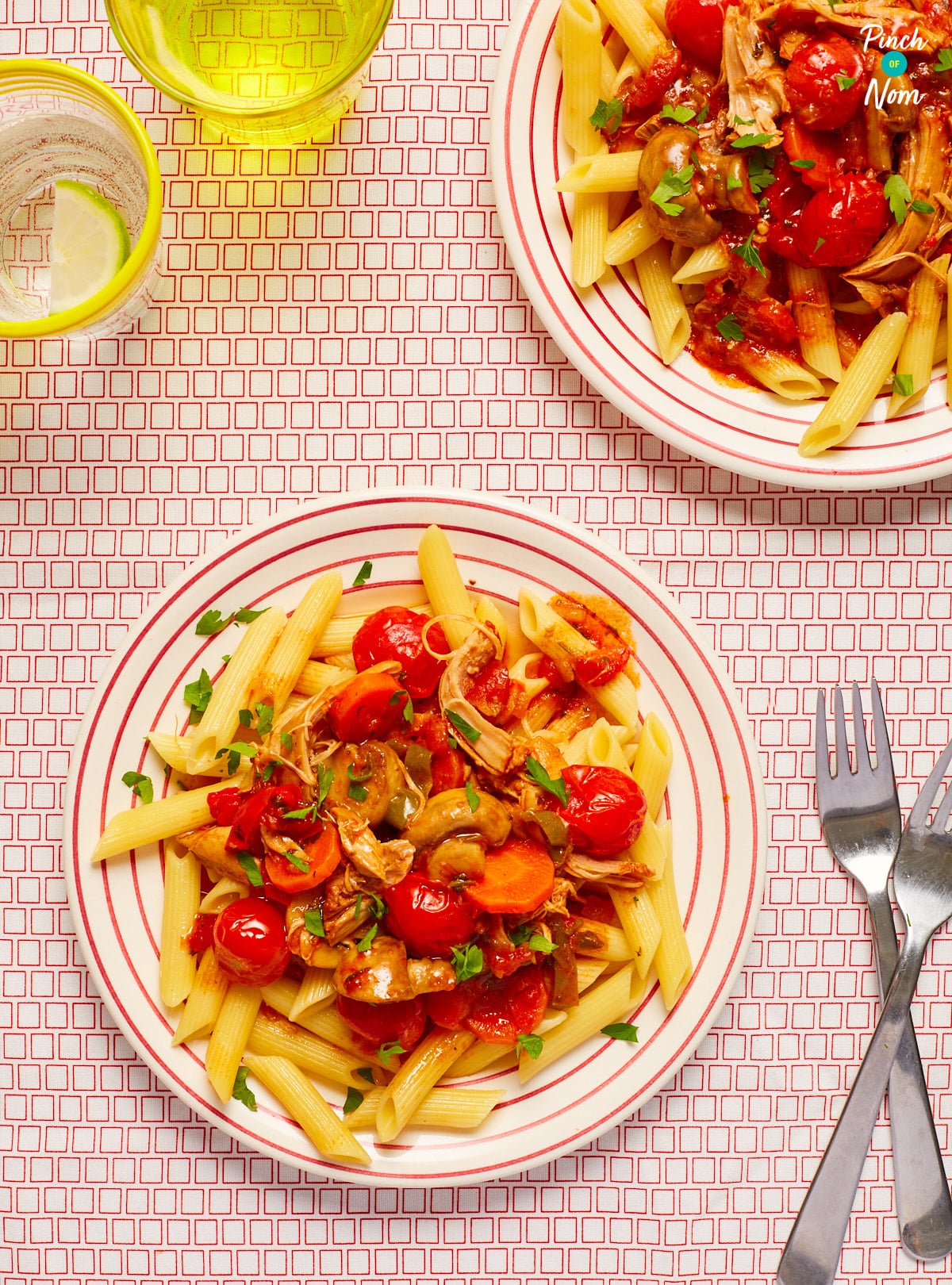 Two servings of Pinch of Nom's Chicken Cacciatore are plated up on a red and white tabletop with forks to the side waiting to tuck in.