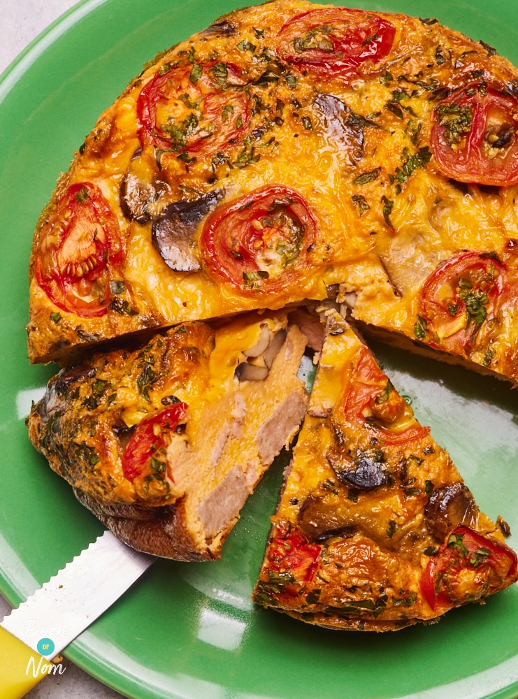 Pinch of Nom's slimming-friendly Breakfast Quiche is served at the centre of a colourful table on a green plate. A slice has been served onto a side plate, with a small bowl of ketchup to the side – ready for dipping!