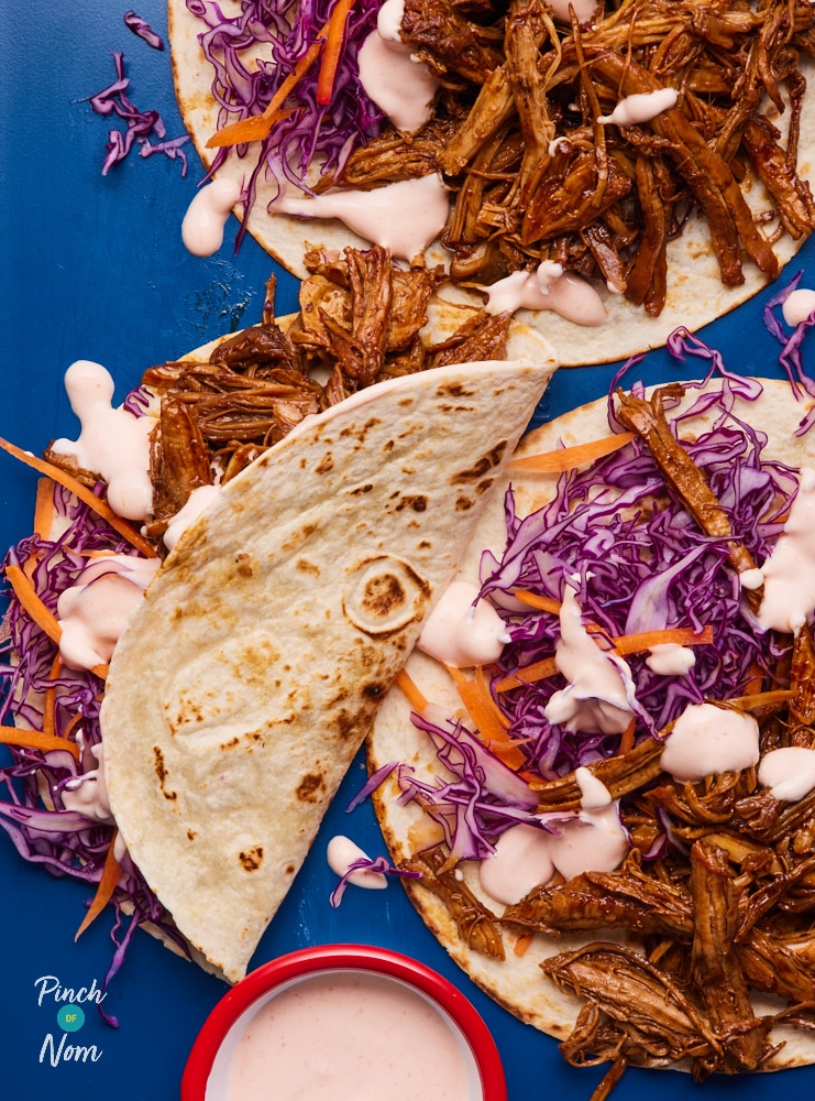 Finished wraps filled with shredded pork, vibrant slaw, and a drizzle of spicy sauce, folded and ready to serve.