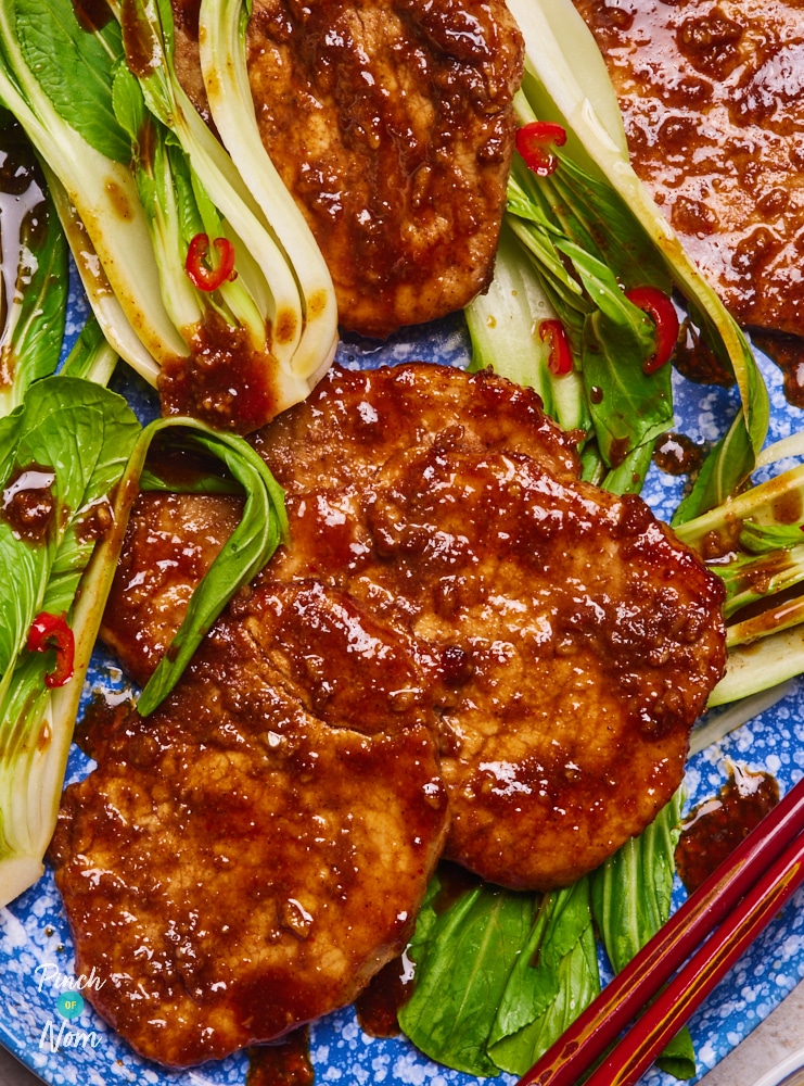 Pinch of Nom's slimming-friendly Sticky Chinese-Style BBQ Pork is served on a blue speckled plate, coated in the juicy glaze over a bed of pak choi. Chopsticks wait to tuck in.