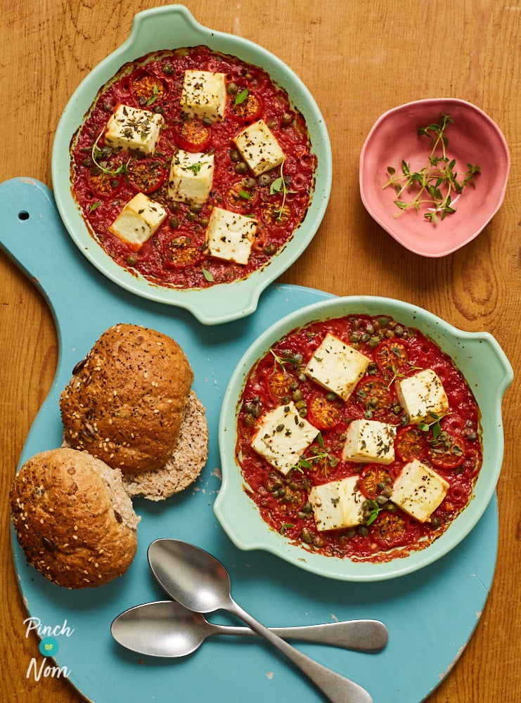 Two small ovenproof dishes are filled with Pinch of Nom's slimming-friendly Baked Feta and Tomatoes recipe, with wholemeal bread rolls waiting to the side for dipping.