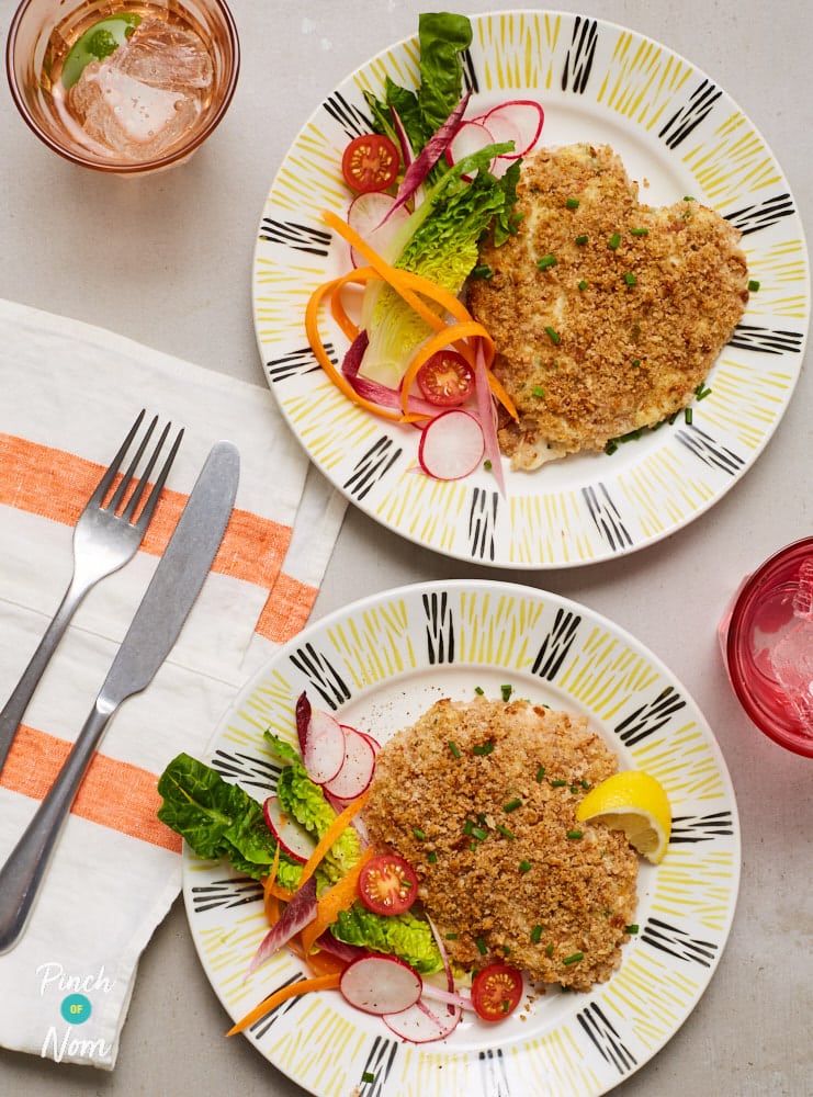 A table is set with two plates of Pinch of Nom's slimming-friendly Cheesy Topped Chicken recipe, with a side of green veggies.