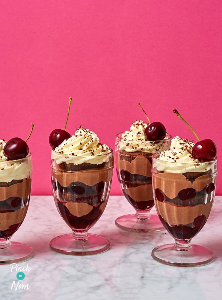 On a marble countertop, four of Pinch of Nom's slimming-friendly Black Forest Desserts are served in tall glasses topped with low-calorie cream and a single cherry each.
