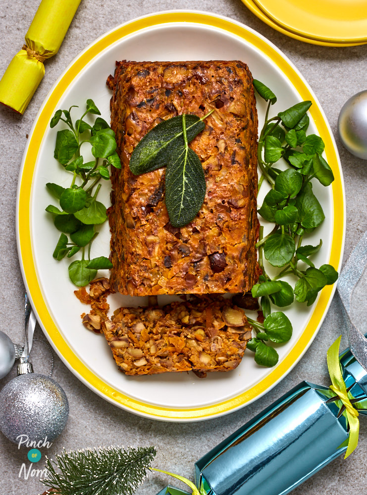 Pinch of Nom's slimming-friendly Chestnut Roast is served on a large serving plate at the centre of a festive dinner table; it has been partially sliced, ready to serve.