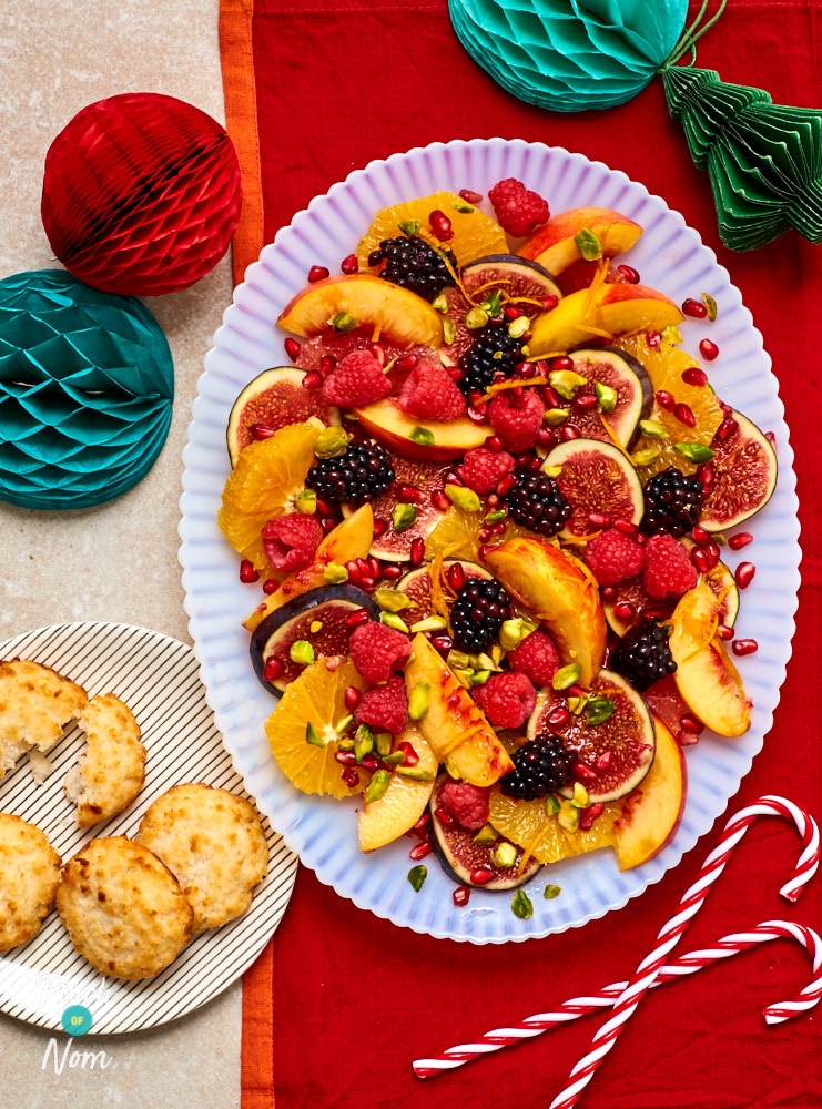 Pinch of Nom's slimming-friendly Festive Fruit Salad is served on a large plate at the centre of a festive table, decorated with candy canes and paper baubles.
