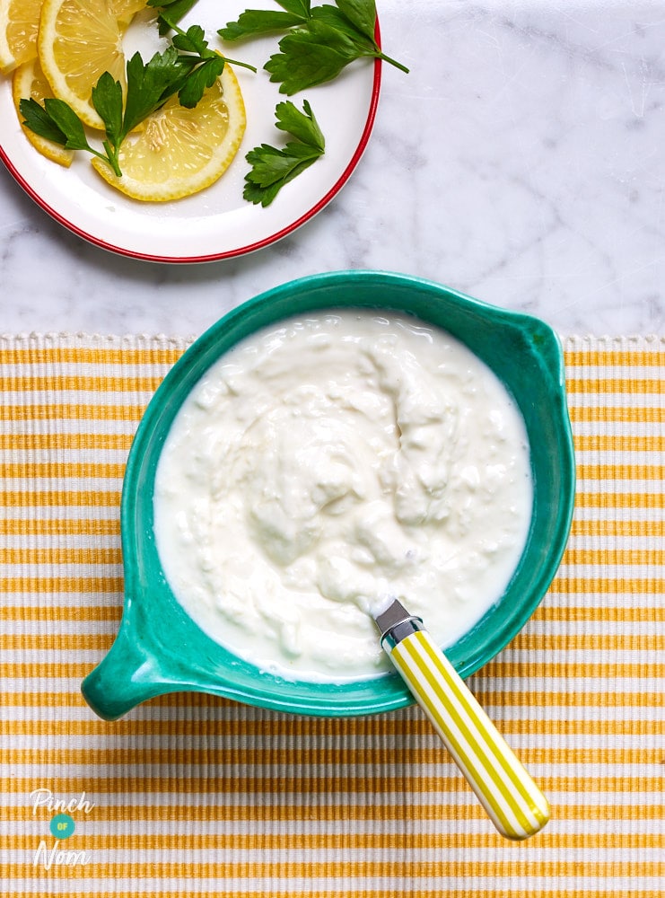 A small dish is filled with Pinch of Nom's slimming-friendly Horseradish Sauce; a spoon is waiting to scoop a dollop onto a plate.