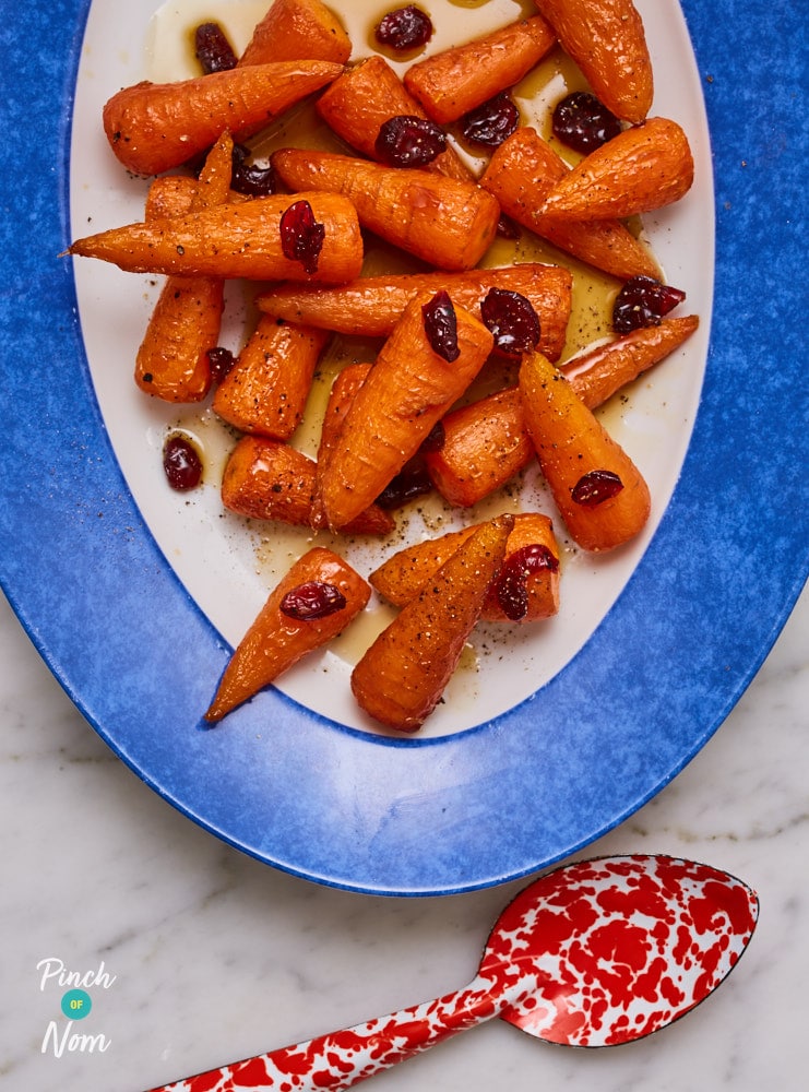 A large serving plate is filled with Pinch of Nom's Maple Glazed Carrots; they're coated in an added drizzle of sticky-sweet sauce and topped with a sprinkling of festive cranberries.