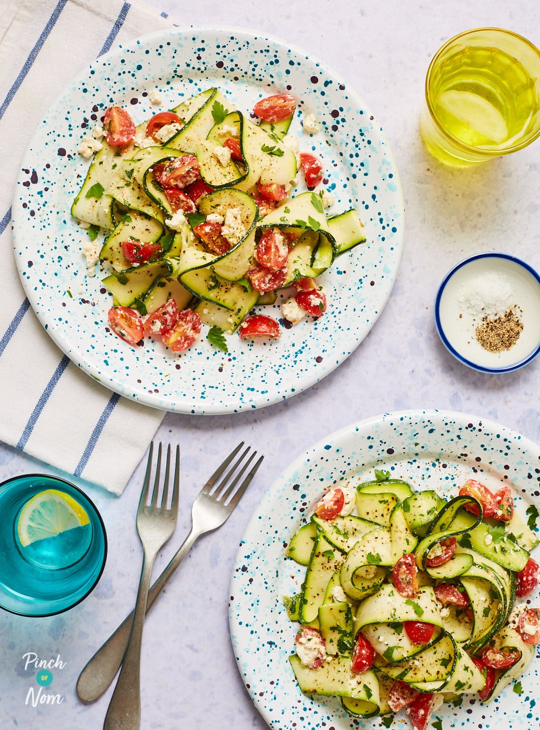 A table is set with two portions of Pinch of. Nom's slimming-friendly Courgette Ribbon, Lemon and Feta Salad.