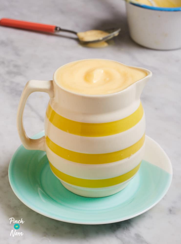 A white and yellow striped jug filled with Pinch of Nom's slimming-friendly Custard is served at the centre of a table.