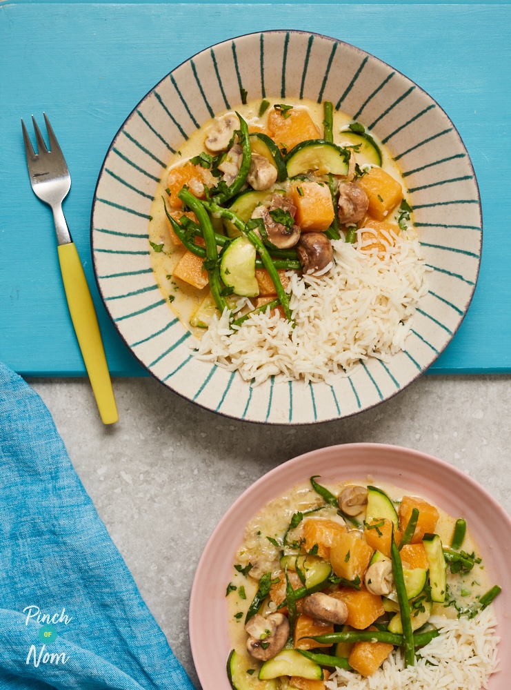 Two portions of Pinch of Nom's Vegetable Coconut Curry are served on a blue tabletop in a large white, striped bowl and on a pink plate. There's a fork to the side ready to dig in.