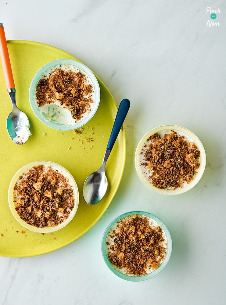 A table is set with four ramekins of Pinch of Nom's Baileys Chocolate Cheesecake Pots - each one is topped with a layer of crunchy biscuits.