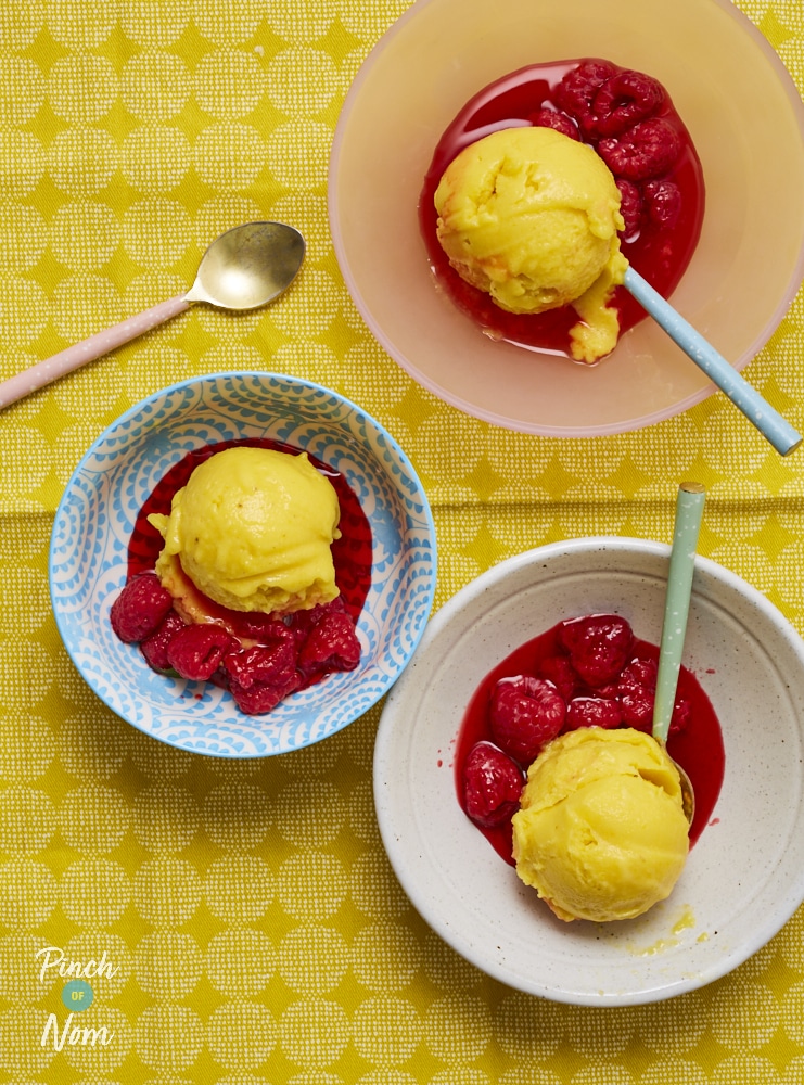 Three bowls are filled with colourful servings of Pinch of Nom's Mango and Raspberry Ice Cream. A spoon is in each bowl, waiting to tuck in. The bright-yellow mango scoop rests on top.