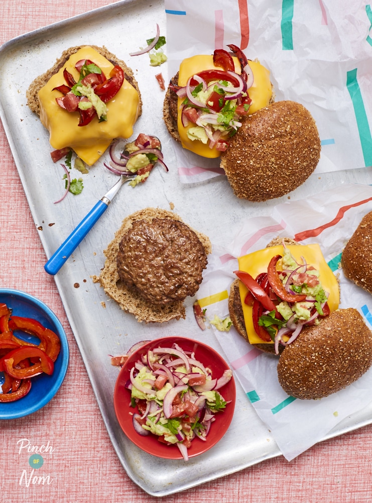 Pinch of Nom's Burrito Burgers are freshly served from the oven on a baking tray, being assembled with cheese slices, roasted peppers and homemade salsa.