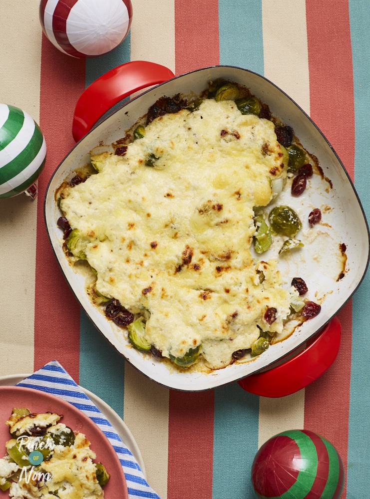 Pinch of Nom's slimming-friendly Cheesy Sprout Bake is served fresh from the oven on a festive-looking colourful table. the cheesy topping is golden brown.