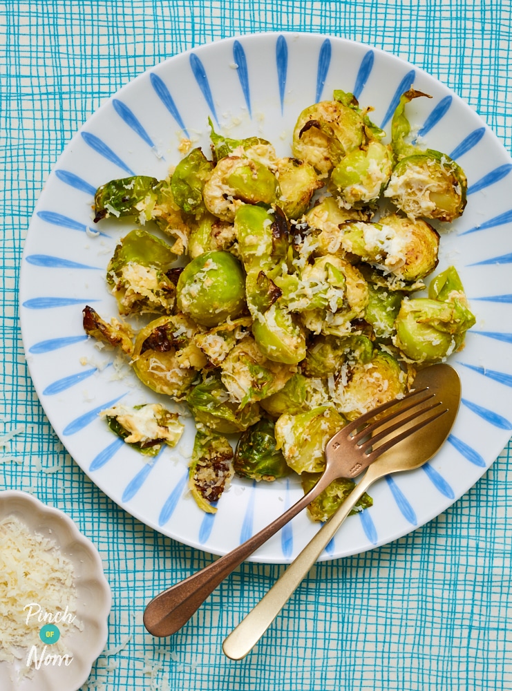 A plate is filled with Pinch of Nom's Creamy Garlic Sprouts waiting to be dished out with two spoons.