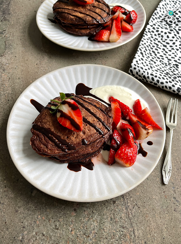 Pinch of Nom's slimming-friendly Chocolate Pancakes are served topped with a chocolate drizzle and sliced strawberries.