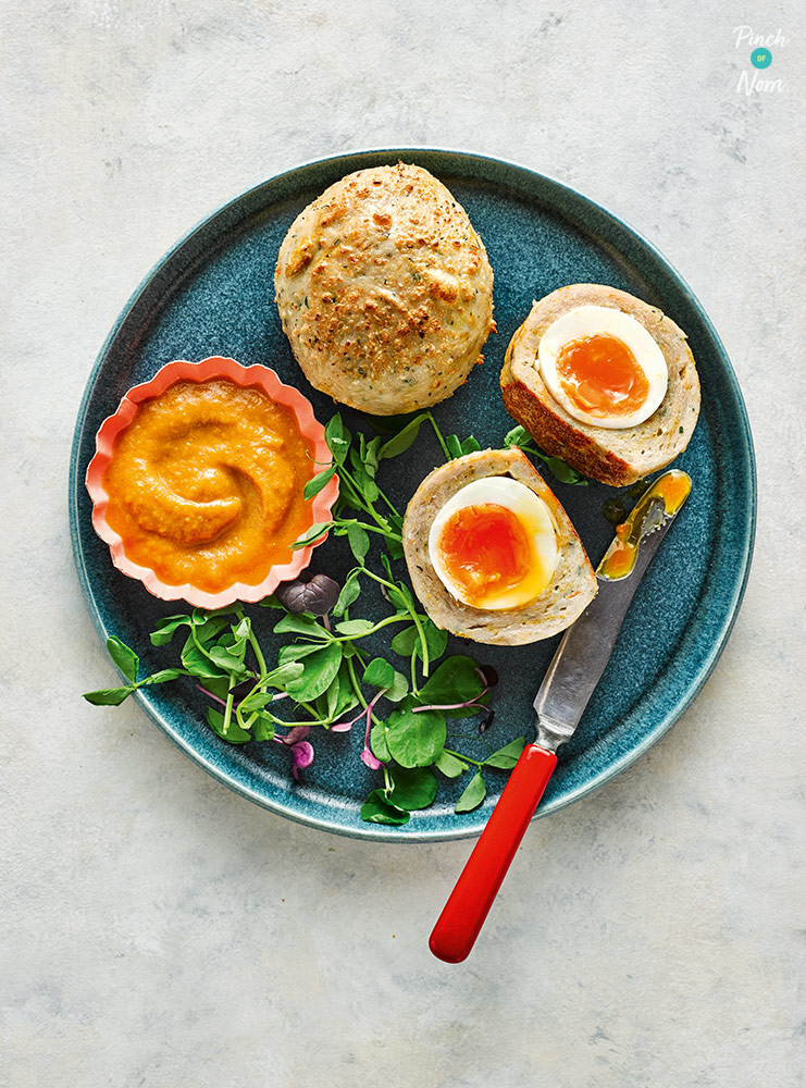 A portion of Pinch of Nom's Katsu Chicken Scotch Eggs from Pinch of Nom: Every Day Light is plated up. One egg has been sliced in half to reveal the runny egg centre; there's a mixed leaf salad and extra Katsu-style dipping sauce to the side. 