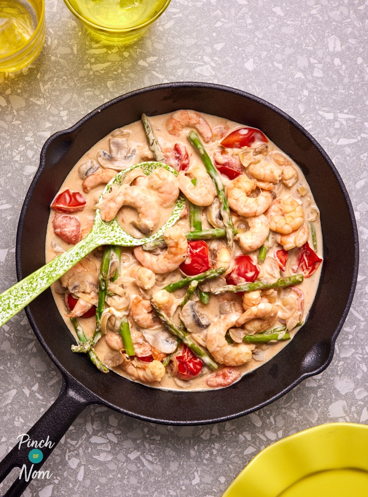 Pinch of Nom's Creamy Garlic Prawns are served in a skillet while a large serving spoon scoops up a creamy portion.