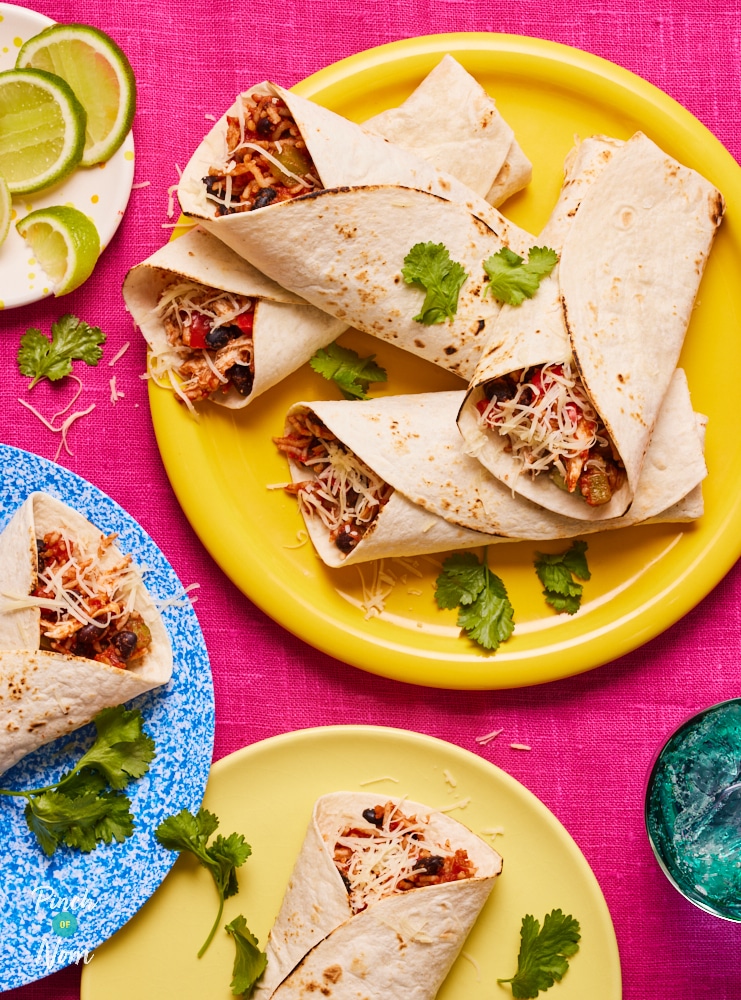 Pinch of Nom's slimming-friendly Chicken Burritos are served plated up on a colourful table with a side of lime wedges.