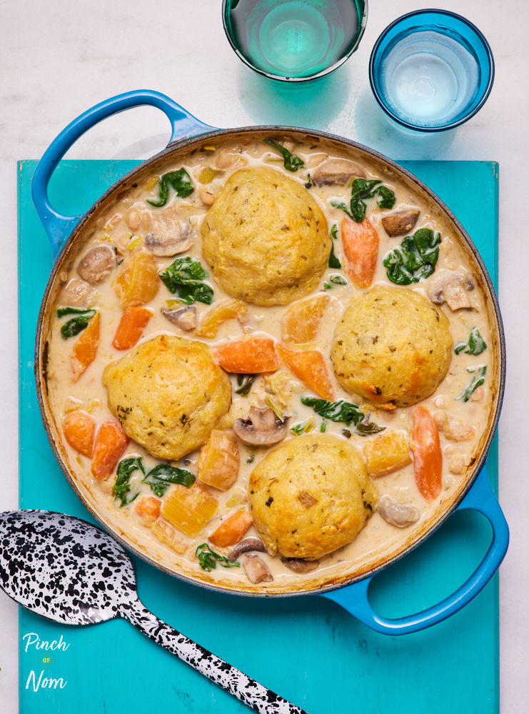 Pinch of Nom's Vegetable Stew with Cheesy Dumplings is at the centre of a table in a bright blue oven dish, waiting to be served with a blue and white speckled spoon.
