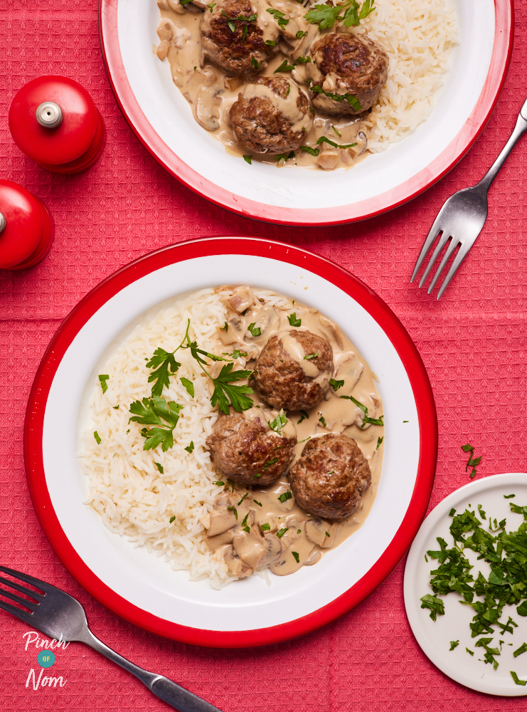 Pinch of Nom's Meatball Stroganoff is plated up on a bright table top. Both portions are served with a fluffy side of basmati rice; parsley leaves are sprinkled on top, and extra leaves are chopped and plated up to the side waiting to be sprinkled, if needed.