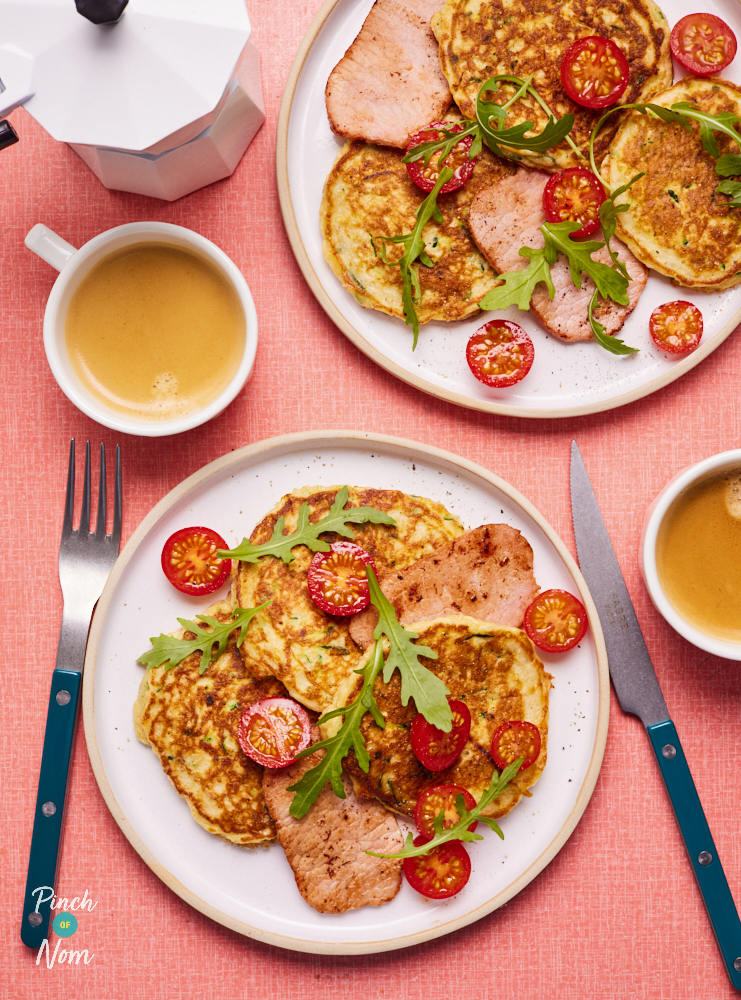 Two portions of Pinch of Nom's Cheesy Courgette Pancakes are plated up as part of a breakfast time spread with two cups of tea.