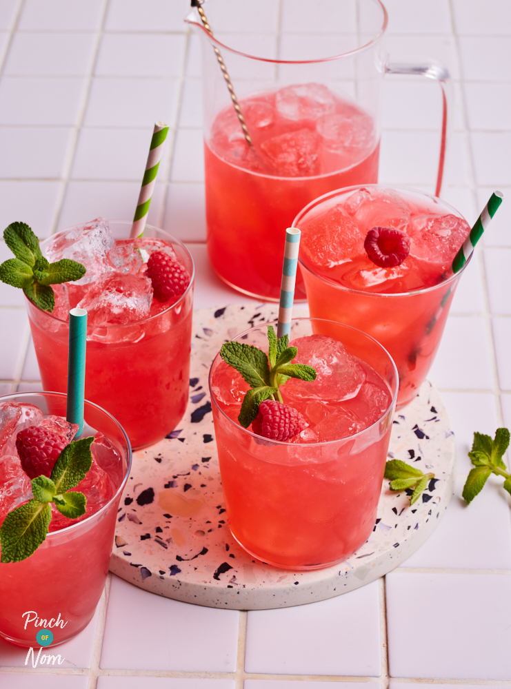 Pinch of Nom's Pink Lemonade is served in 4 glasses over ice with striped paper straws, fresh raspberries and a sprig of fresh mint.