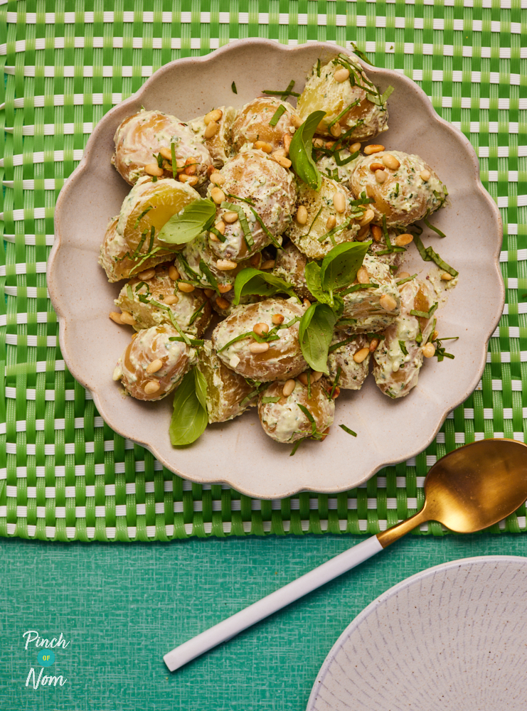 Pinch of Nom's Pesto Potato Salad is plated up on a bright green table with a spoon waiting to dig in.