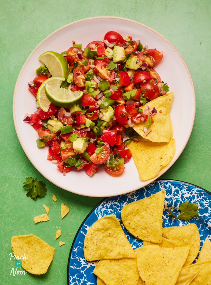 A plate of Pinch of Nom's colourful Salsa Salad is served with lime wedges waiting to be squeezed over, and low-calorie tortilla chips on a side plate ready to scoop up every last bit.