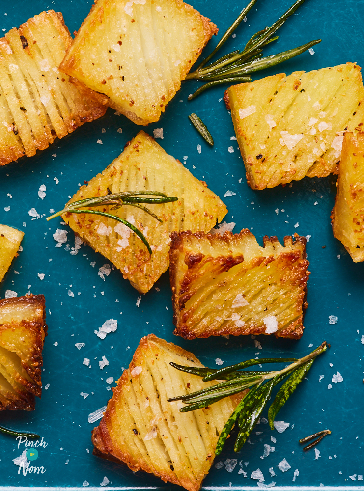 A close up of a tray of golden brown Accordion Potatoes. The rectangular potatoes are crispy at the edges, sprinkled with sea salt and fresh herbs.