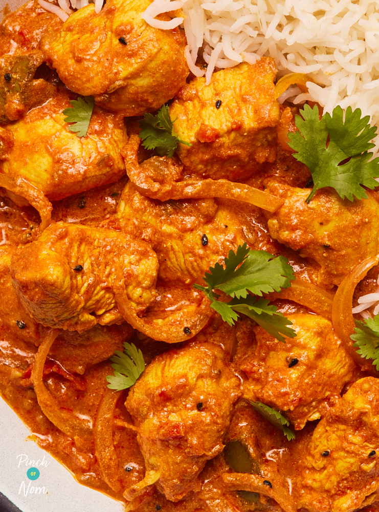 A close up of Pinch of Nom's Chicken and Mango Pickle Curry. It is served with white basmati rice and garnished with fresh herbs.