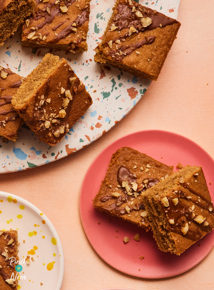 A close-up of slices from Pinch of Nom's Coffee and Walnut Sponge Traybake, drizzled with coffee icing and chopped walnuts.