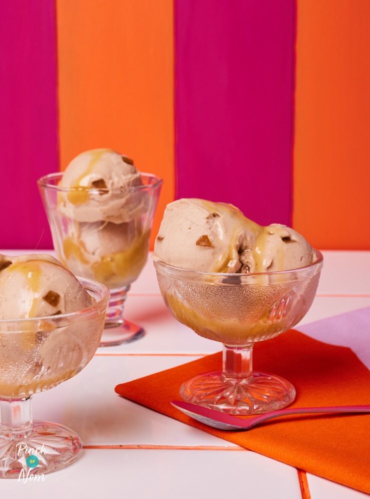 A table is placed against a bright pink and orange striped background. On the table, 3 portions of Pinch of Nom's low-calorie Ninja Creami Banoffee Ice Cream have been served in glass ice cream bowls. Each scoop of creamy ice cream is drizzled with toffee sauce.