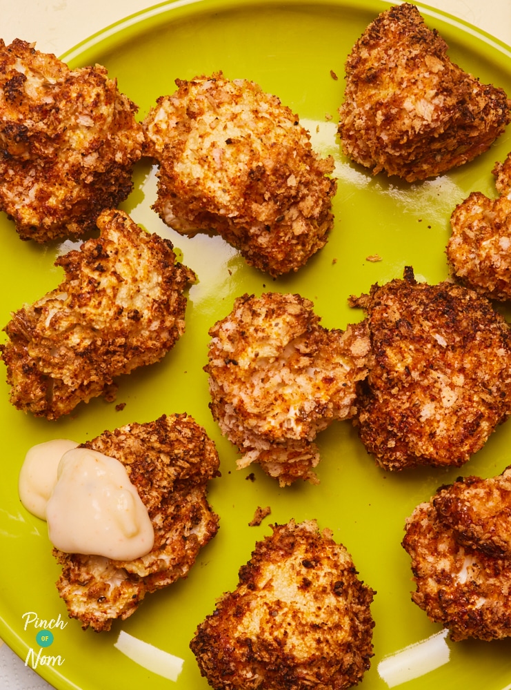 Pinch of Nom's slimming-friendly Air Fryer Cauliflower Cheese Florets are served freshly-baked and golden brown on a bright green plate, with a dollop of cheesy dipping sauce coating one of the florets.