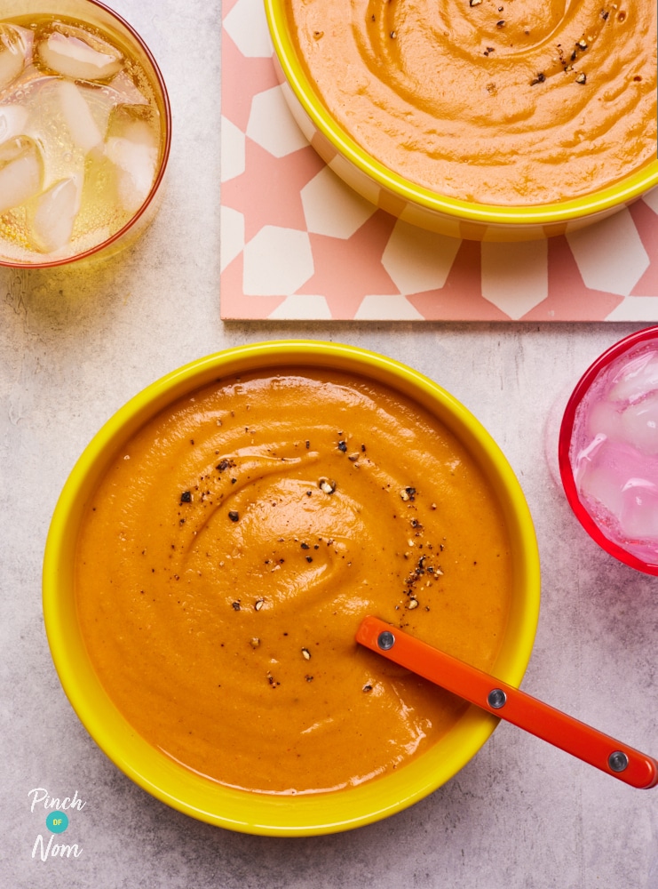 A table is set with two eye-catching bowls of Pinch of Nom's slimming-friendly Sweet Potato and Red Lentil Soup, each bowl is topped with a sprinkling of cracked black pepper.