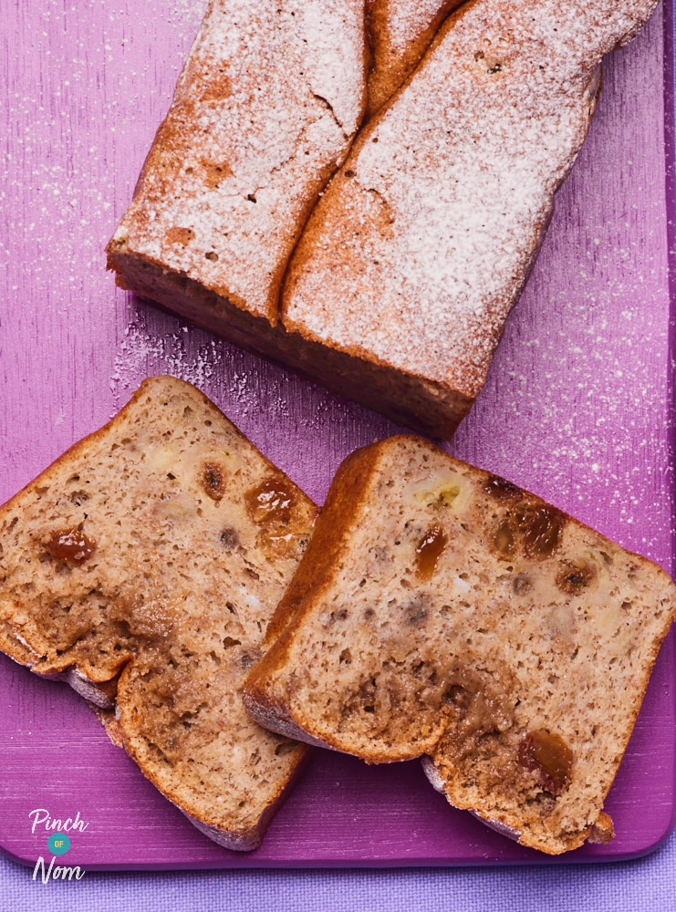 Pinch of Nom's slimming-friendly Banana Bread Pudding is partially sliced and served on a bright purple chopping board.