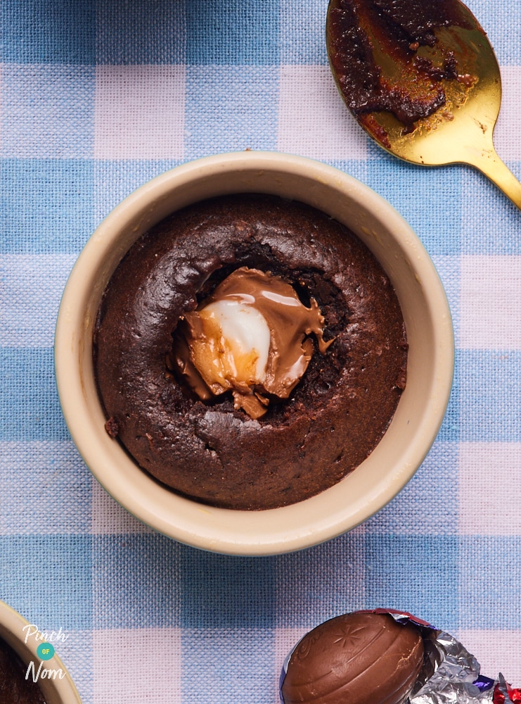 One of Pinch of Nom's slimming-friendly Creme Egg Lava Cakes is served in a ramekin with part of the sponge removed, revealing the gooey-in-the-middle creme egg centre.