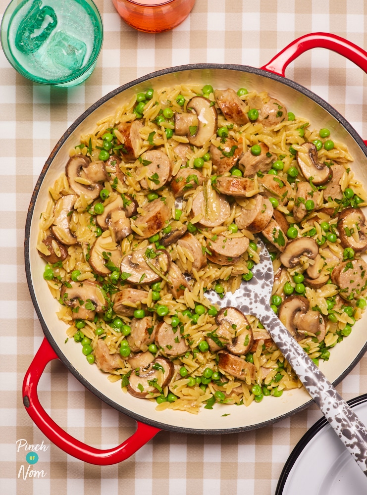 A large ovenproof casserole dish is filled with Pinch of Nom's slimming-friendly Herby Sausage Orzo,. A large serving spoon is beginning to scoop out a portion, ready to start dishing out.