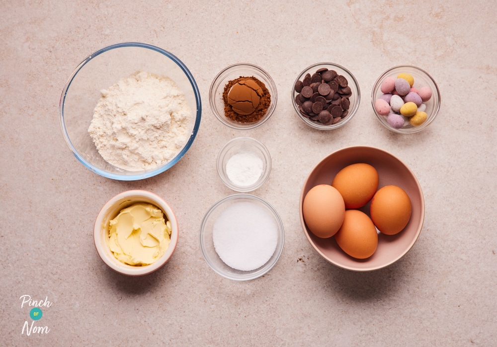 The raw ingredients for Pinch of Nom's Mini Egg Brownies are laid out on a kitchen counter, ready to begin baking.