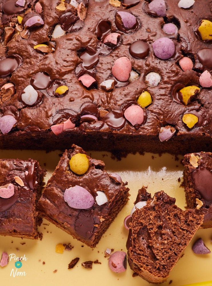 A chopping board is topped with a freshly-baked batch of Pinch of Nom's slimming-friendly Easter Mini Egg Brownies.