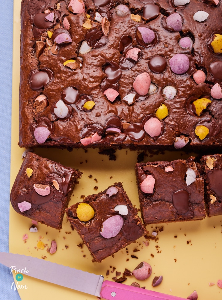A chopping board is topped with a freshly-baked batch of Pinch of Nom's slimming-friendly Easter Mini Egg Brownies.
