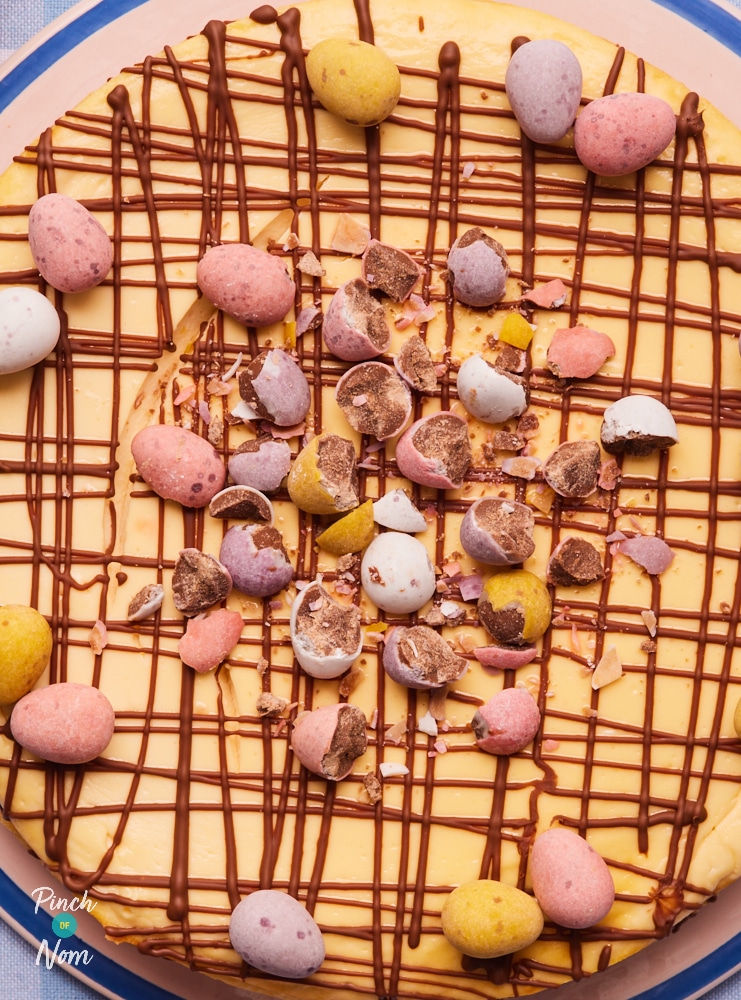 Pinch of Nom's slimming-friendly Mini Egg Cheesecake topped with a chocolate drizzle and colourful mini eggs.