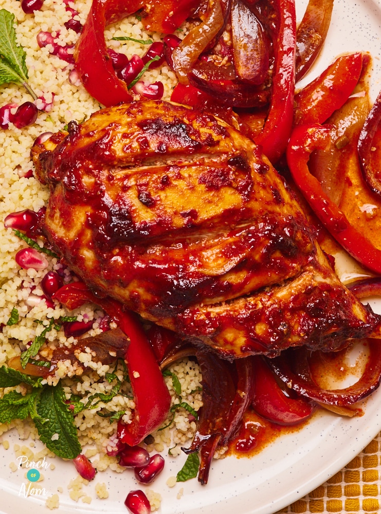 Pinch of Nom's slimming-friendly Pomegranate and Harissa Chicken is served on a bed of sliced peppers and onions, with a side of fluffed up couscous.