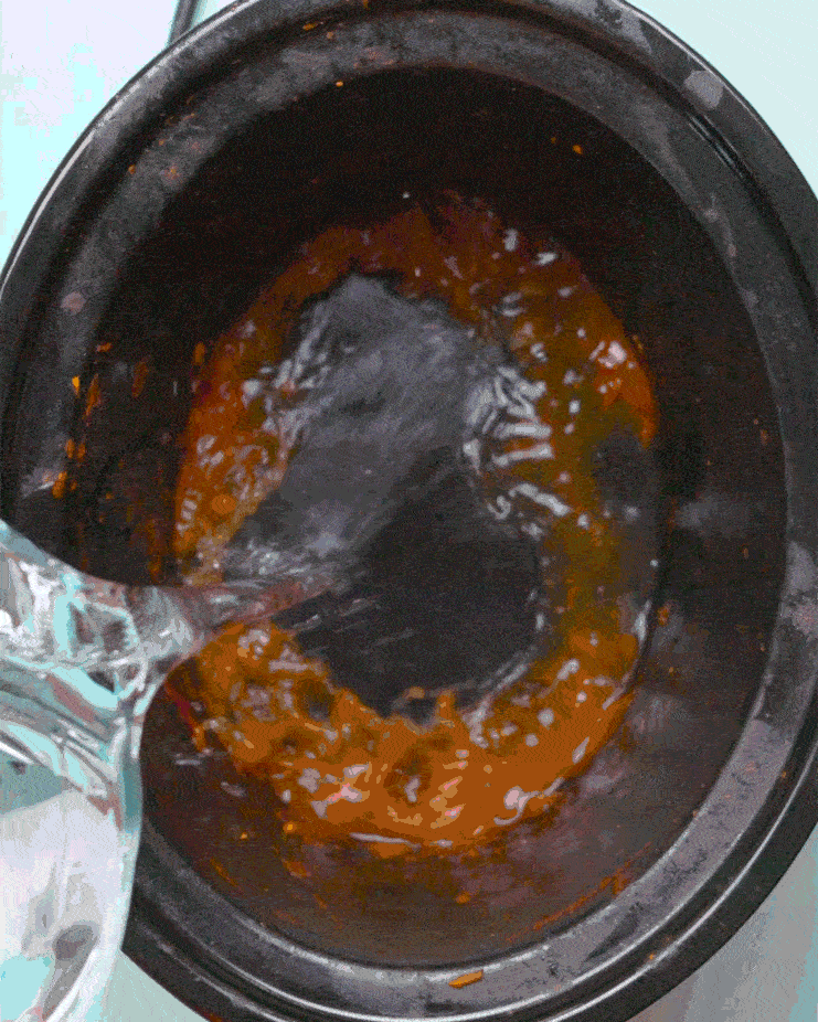 Warm water is poured into a grimy slow cooker pot.