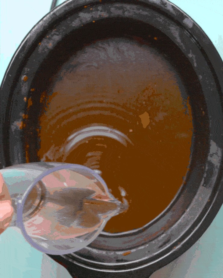 White vinegar is poured into a grimy slow cooker pot.