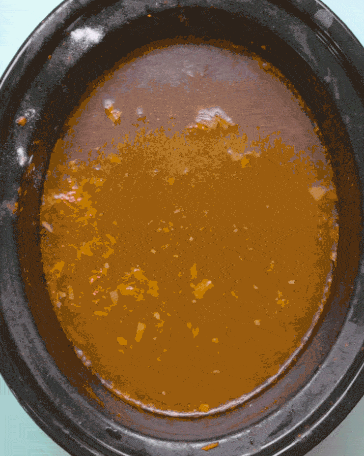 Baking soda is poured into a grimy slow cooker pot filled with warm water and vinegar.