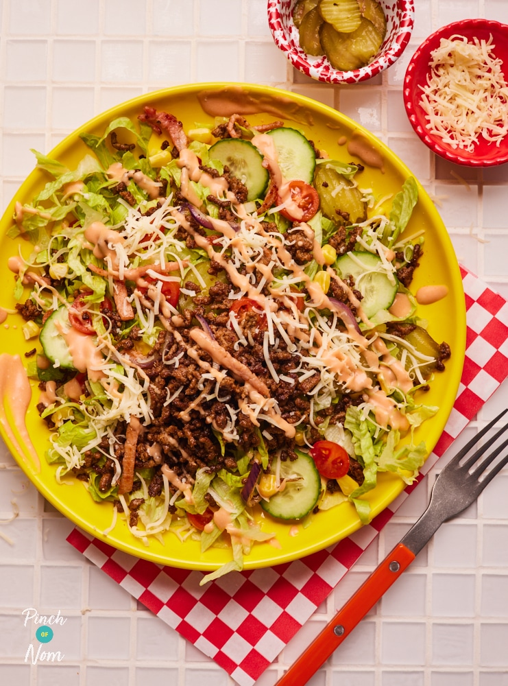 A plate is topped with a colourful, slimming-friendly serving of Pinch of Nom's Cheeseburger Chopped Salad. All topped off with a drizzle of homemade burger sauce.