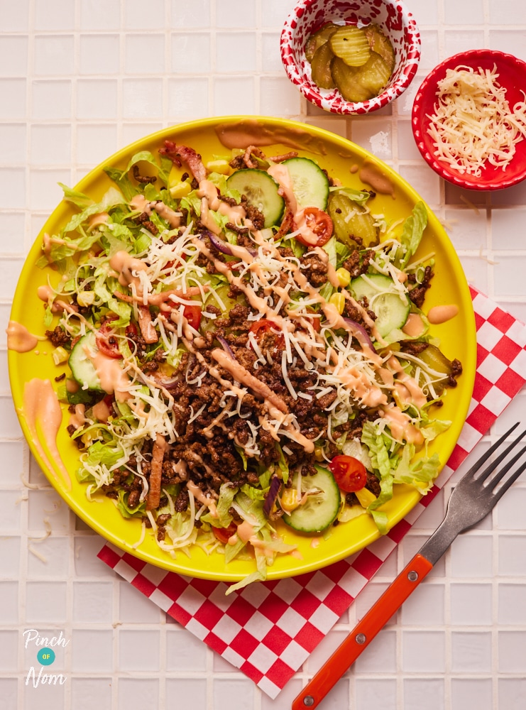 A plate is topped with a colourful, slimming-friendly serving of Pinch of Nom's Cheeseburger Chopped Salad. All topped off with a drizzle of homemade burger sauce.
